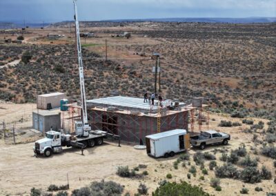 Construction site in a desert landscape with a tall crane, scaffolding, and trucks around a partially built structure.