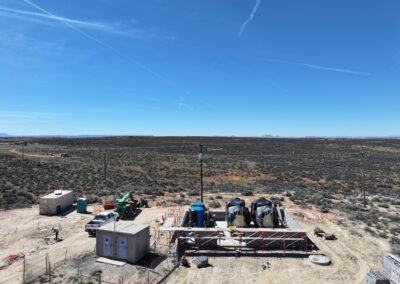 Construction site in a desert landscape with equipment, containers, and power lines under a clear blue sky.